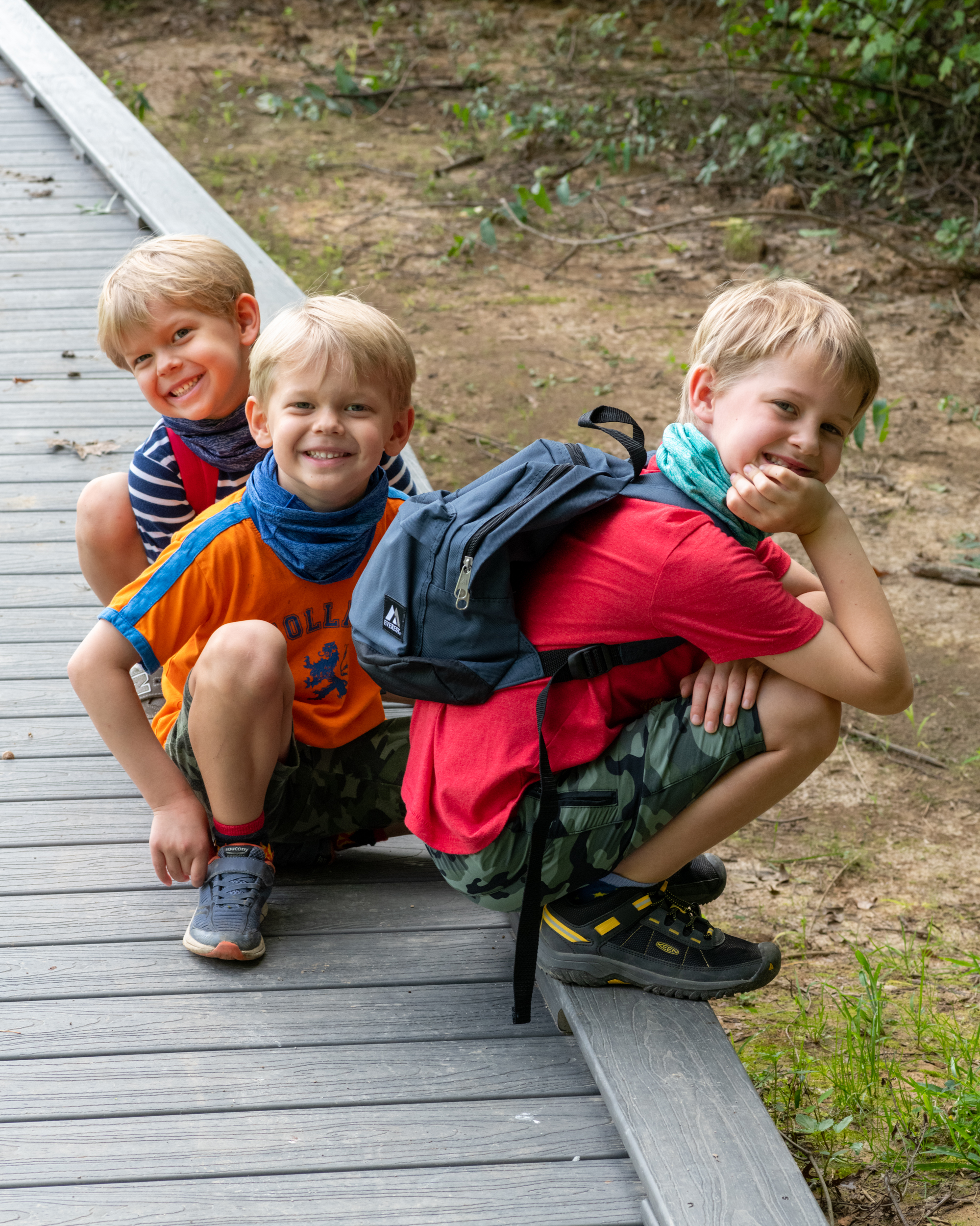 Three young boys crouch together on a boardwalk